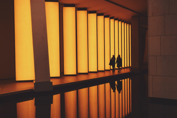 Two figures navigate an orange-lit city street, symbolizing the interconnectedness of global financial markets covered in Integral's news.